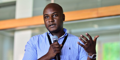 Young, black male with blue business shirt, speaks with a microphone